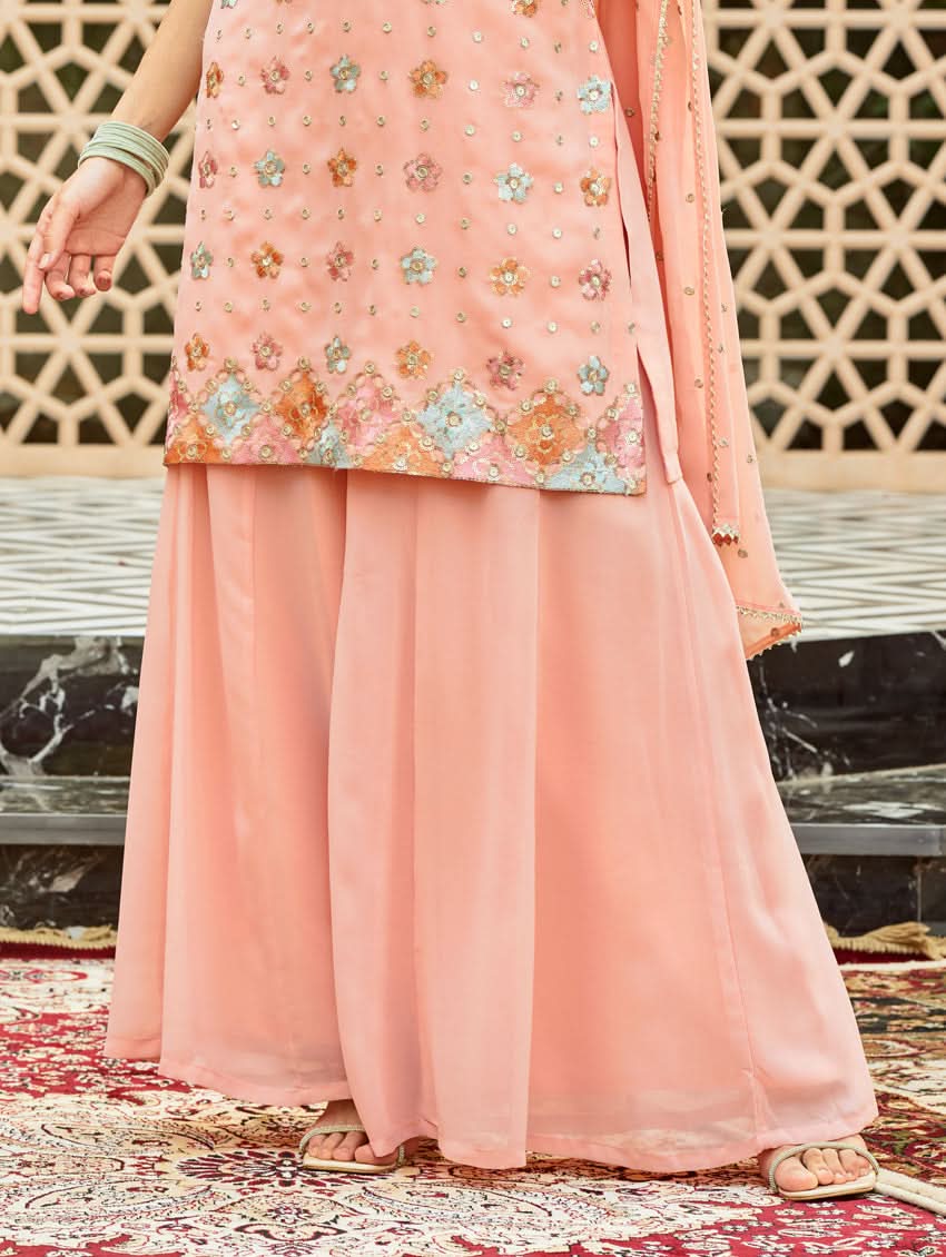 A model wearing a pink embroidered georgette sharara suit set with a round neckline and sleeveless design, featuring sequin work and a dupatta.