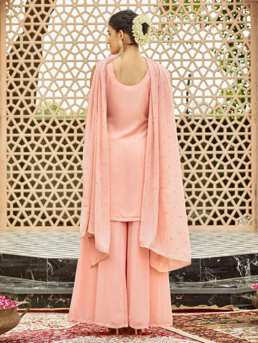 A model wearing a pink embroidered georgette sharara suit set with a round neckline and sleeveless design, featuring sequin work and a dupatta.
