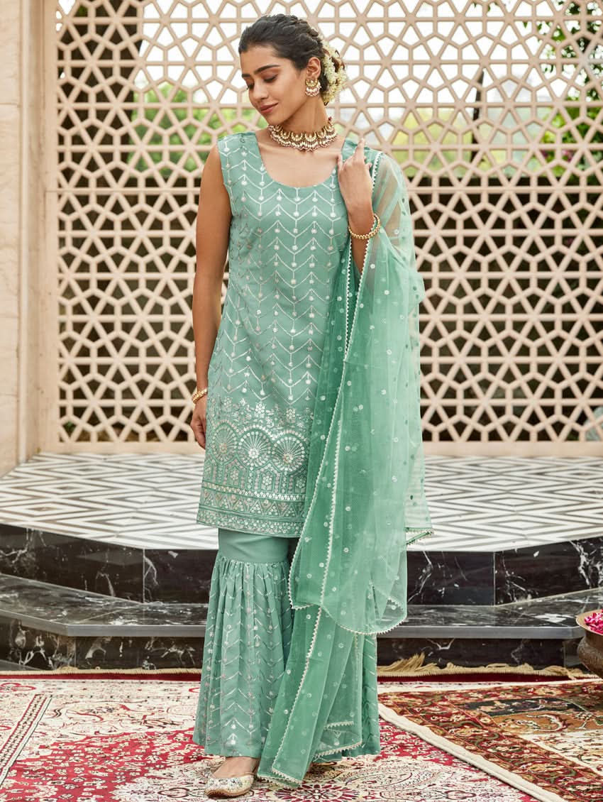 A woman wearing an embroidered Georgette Gharara suit set with a dupatta, featuring a round neckline, sleeveless design, and elasticated waistband. The set is in a teal blue color.