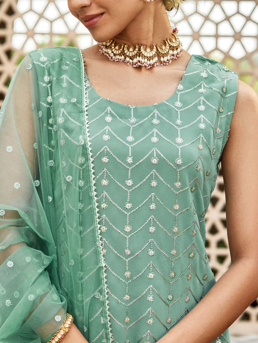 A woman wearing an embroidered Georgette Gharara suit set with a dupatta, featuring a round neckline, sleeveless design, and elasticated waistband. The set is in a teal blue color.