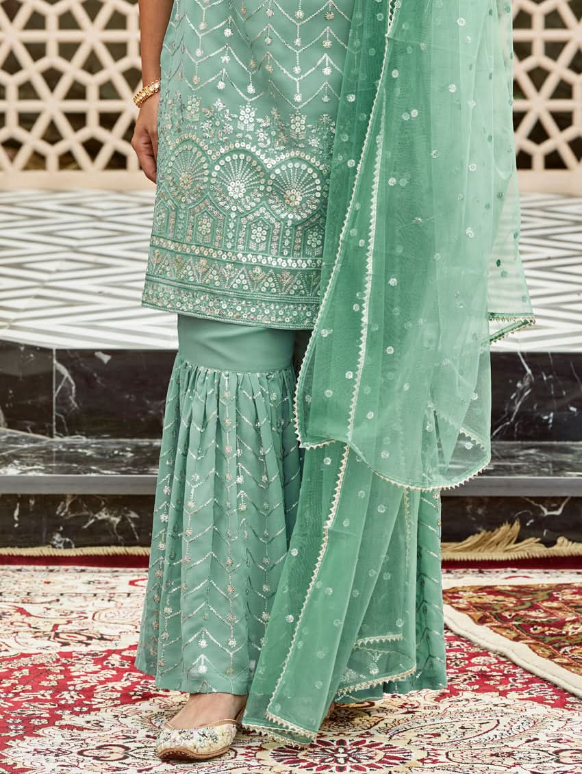 A woman wearing an embroidered Georgette Gharara suit set with a dupatta, featuring a round neckline, sleeveless design, and elasticated waistband. The set is in a teal blue color.
