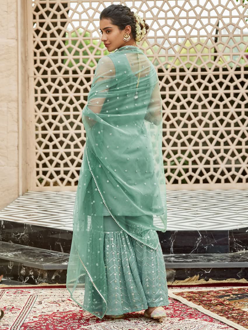 A woman wearing an embroidered Georgette Gharara suit set with a dupatta, featuring a round neckline, sleeveless design, and elasticated waistband. The set is in a teal blue color.