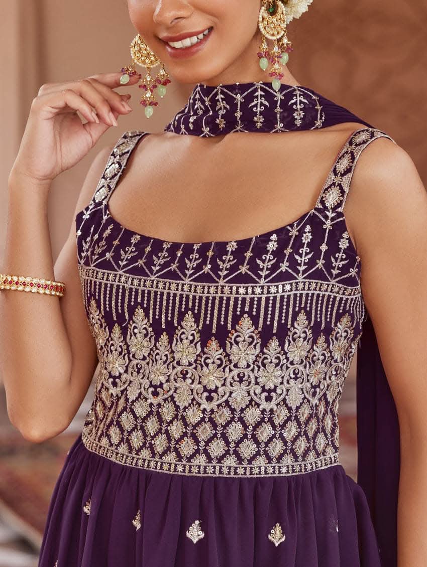 A woman wearing a purple peplum style suit set with embroidered kurta and sharara, standing in a beautifully decorated area.