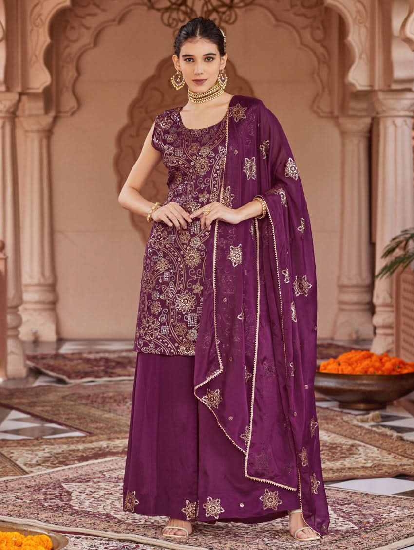 A woman wearing a traditional purple Georgette suit set with embroidered sequins, consisting of a kurta with round neckline and sleeveless design, and a sharara with an elasticated waistband. The set is complemented by a dupatta.
