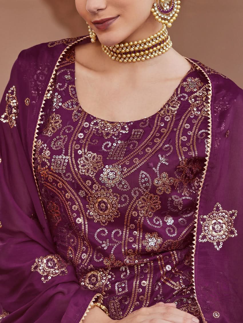 A woman wearing a traditional purple Georgette suit set with embroidered sequins, consisting of a kurta with round neckline and sleeveless design, and a sharara with an elasticated waistband. The set is complemented by a dupatta.
