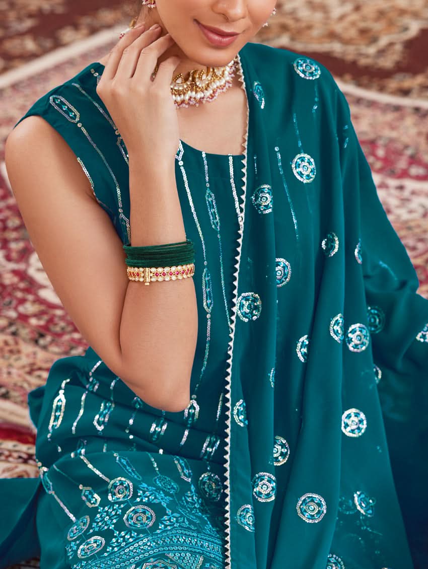 A woman wearing a traditional green Georgette suit set with embroidered sequins, consisting of a kurta with round neckline and sleeveless design, and a sharara with an elasticated waistband. The set is complemented by a dupatta.