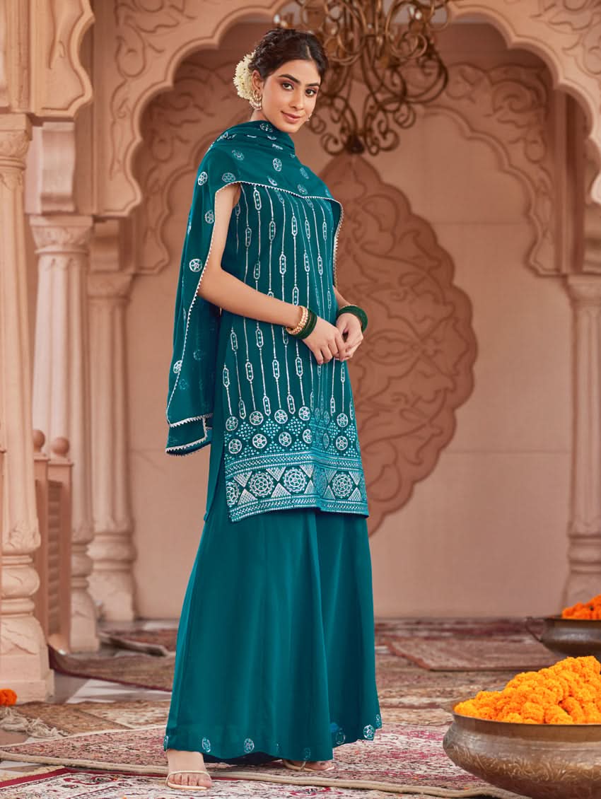 A woman wearing a traditional green Georgette suit set with embroidered sequins, consisting of a kurta with round neckline and sleeveless design, and a sharara with an elasticated waistband. The set is complemented by a dupatta.