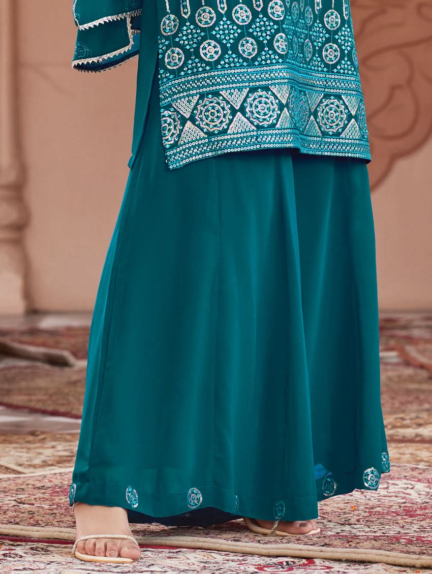 A woman wearing a traditional green Georgette suit set with embroidered sequins, consisting of a kurta with round neckline and sleeveless design, and a sharara with an elasticated waistband. The set is complemented by a dupatta.