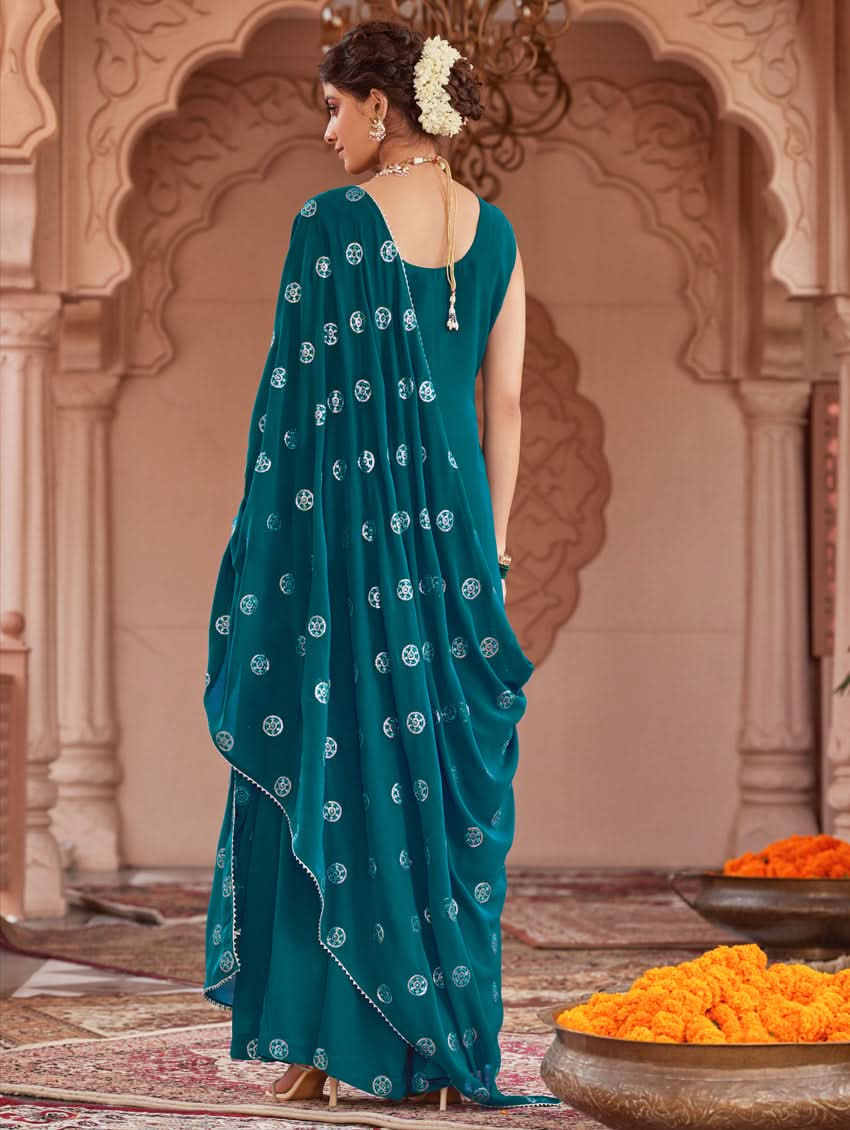 A woman wearing a traditional green Georgette suit set with embroidered sequins, consisting of a kurta with round neckline and sleeveless design, and a sharara with an elasticated waistband. The set is complemented by a dupatta.