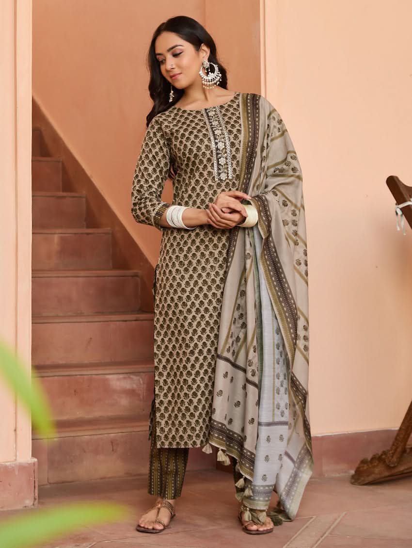 A woman standing on a staircase wearing a beige and green printed cotton suit set with a dupatta.