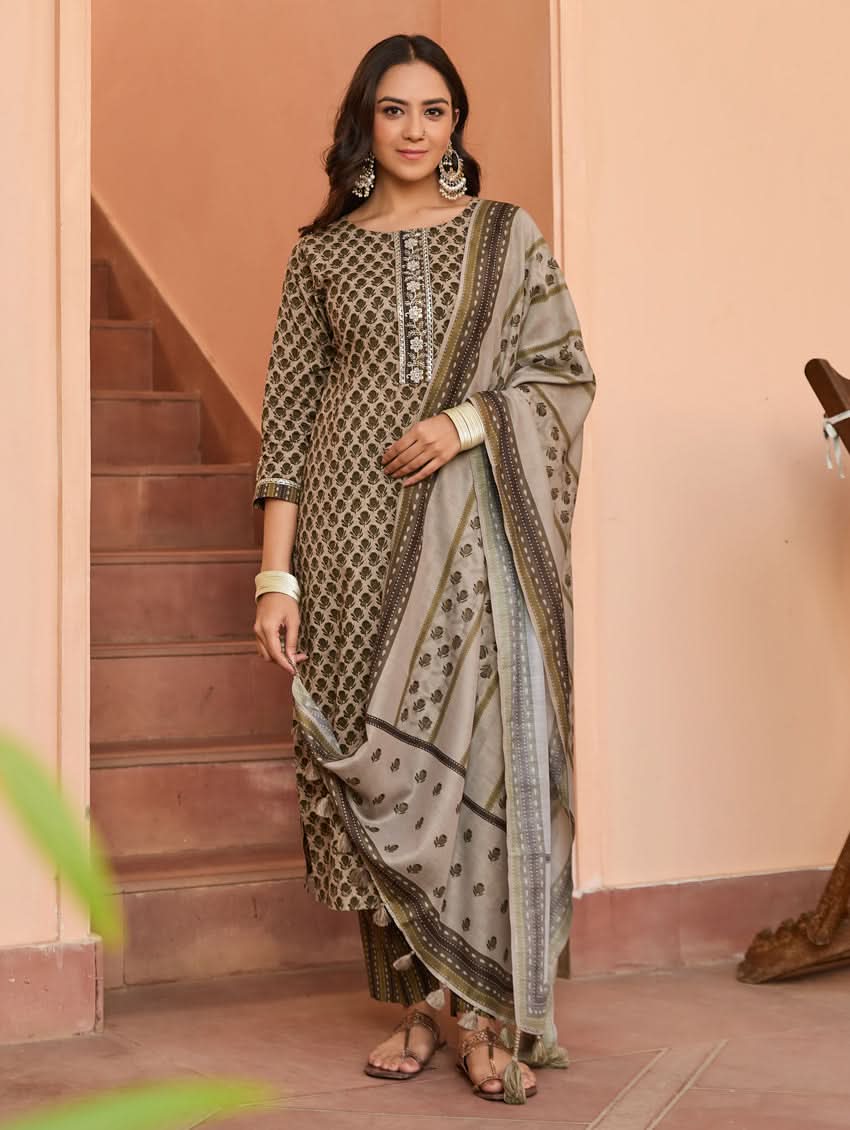 A woman standing on a staircase wearing a beige and green printed cotton suit set with a dupatta.