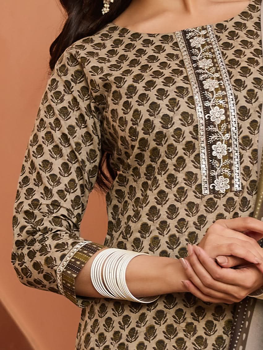 A woman standing on a staircase wearing a beige and green printed cotton suit set with a dupatta.