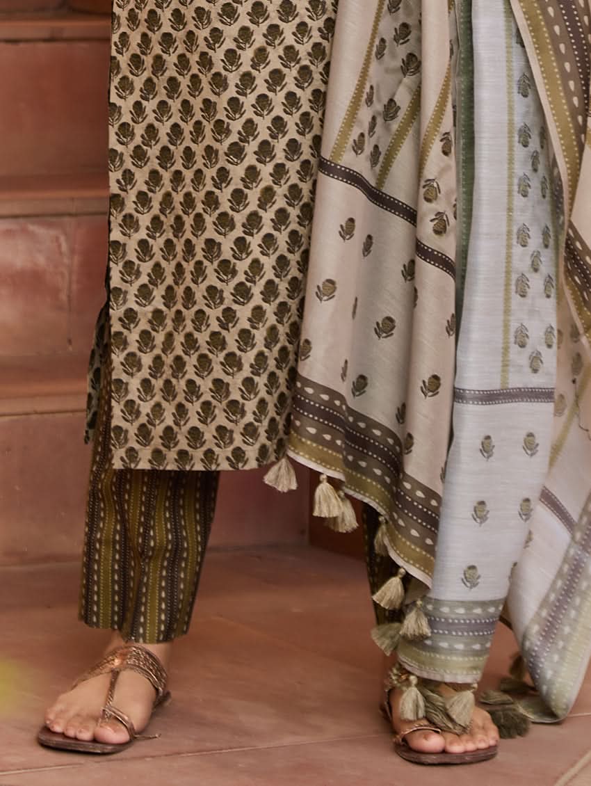 A woman standing on a staircase wearing a beige and green printed cotton suit set with a dupatta.