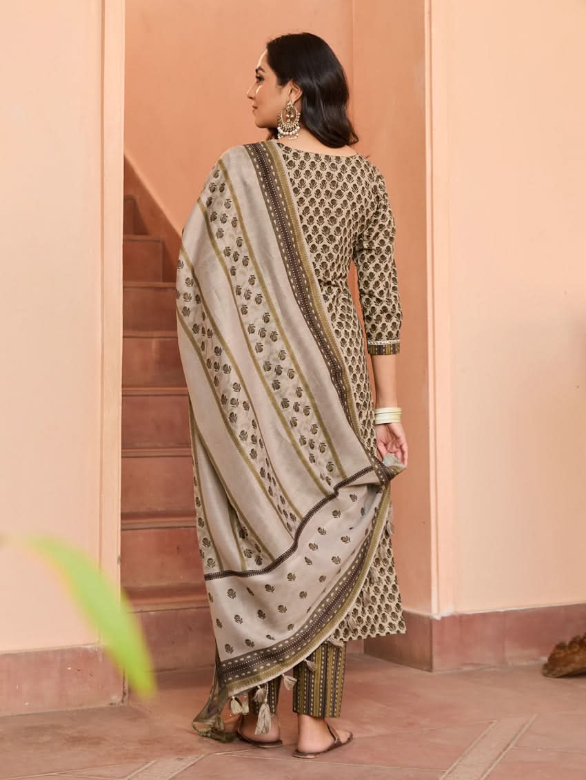 A woman standing on a staircase wearing a beige and green printed cotton suit set with a dupatta.