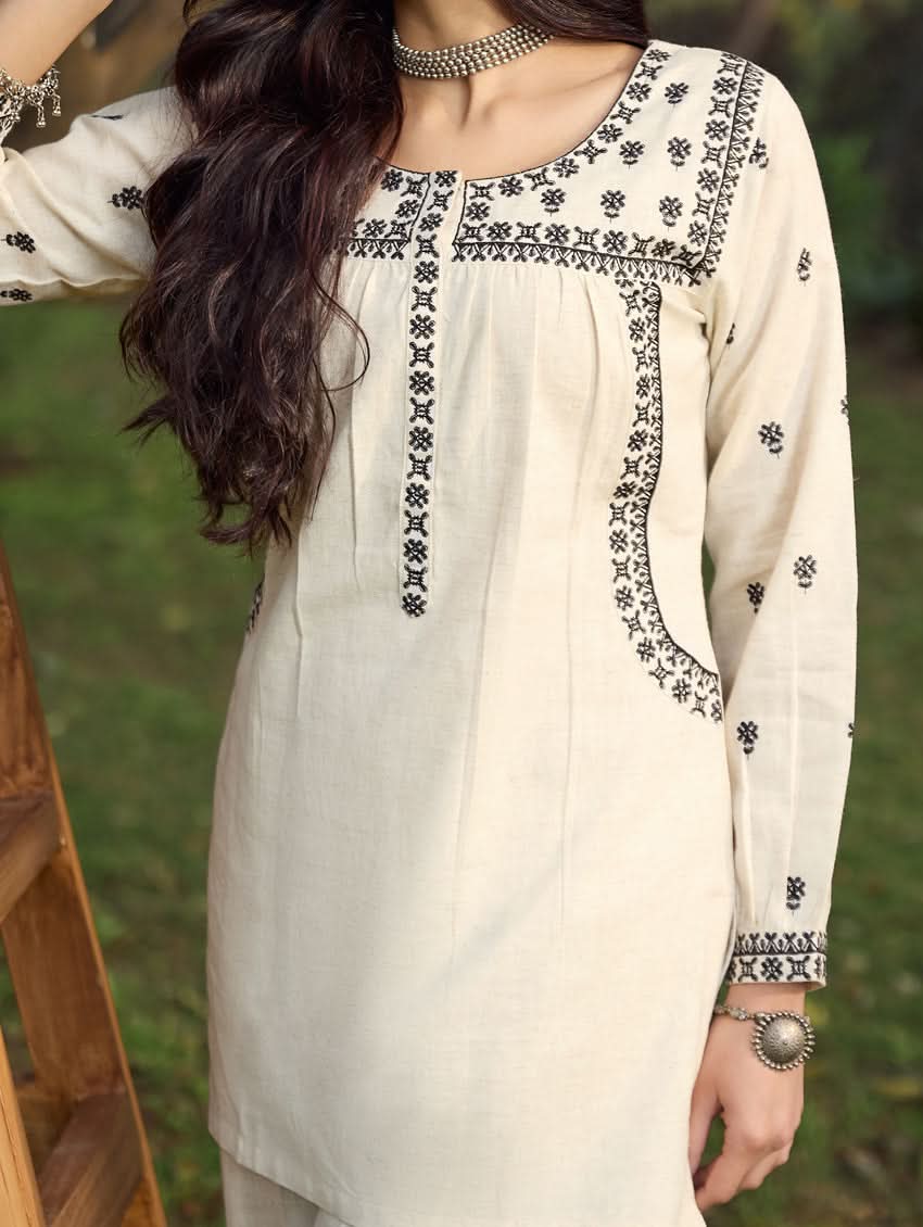A woman standing outdoors wearing a beige embroidered viscose flex co-ord set with short kurta and pants, next to a pink bicycle.