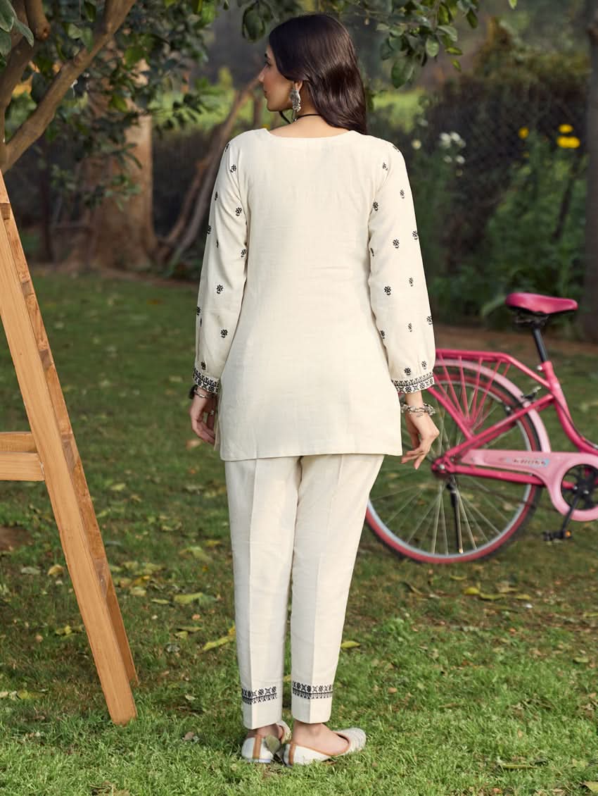 A woman standing outdoors wearing a beige embroidered viscose flex co-ord set with short kurta and pants, next to a pink bicycle.