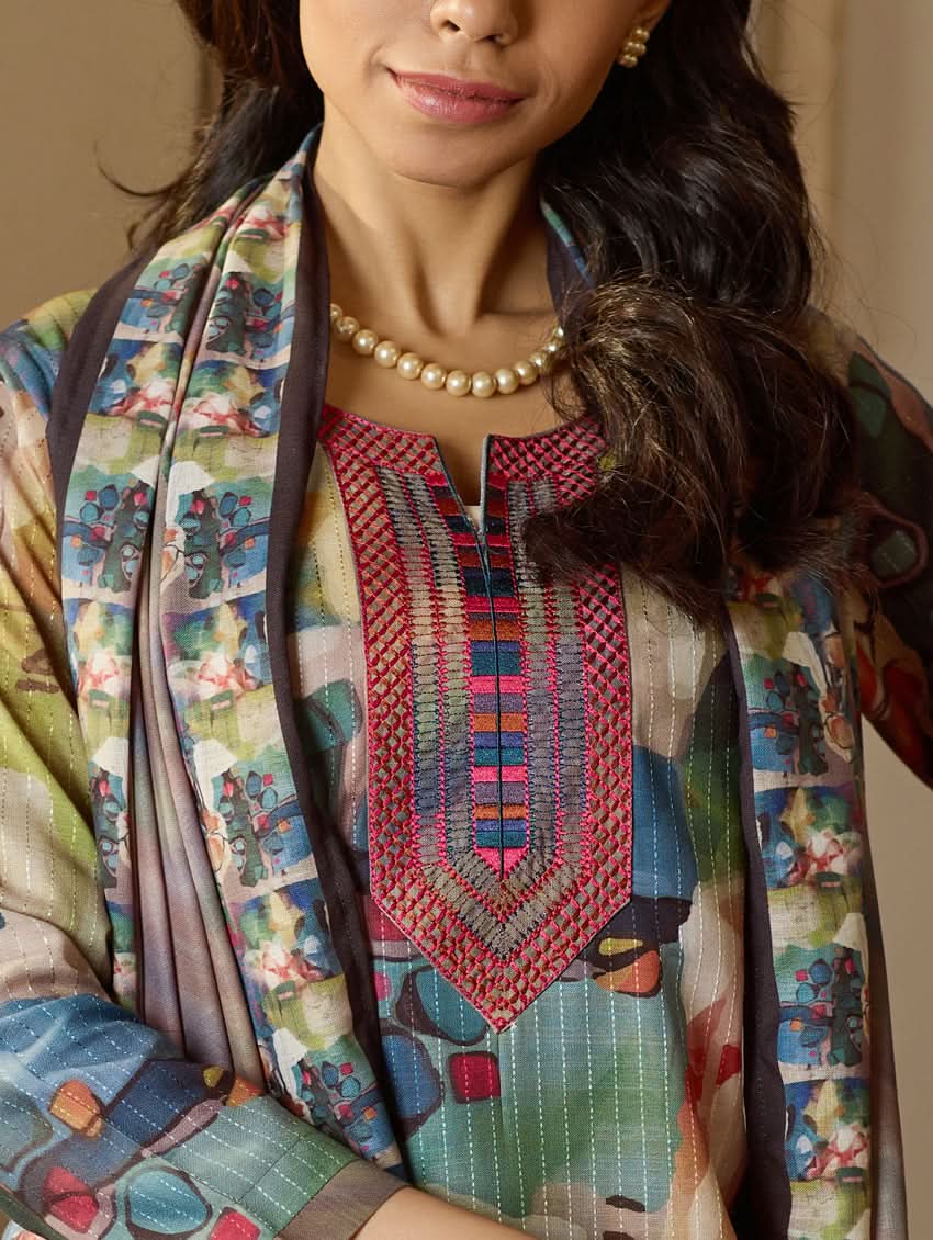 A woman wearing a floral digitally printed cotton suit set with a kurta, pants, and a dupatta, standing in a room with wooden furniture.