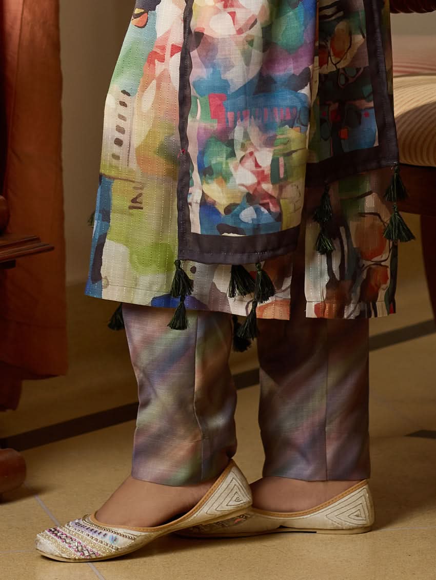 A woman wearing a floral digitally printed cotton suit set with a kurta, pants, and a dupatta, standing in a room with wooden furniture.