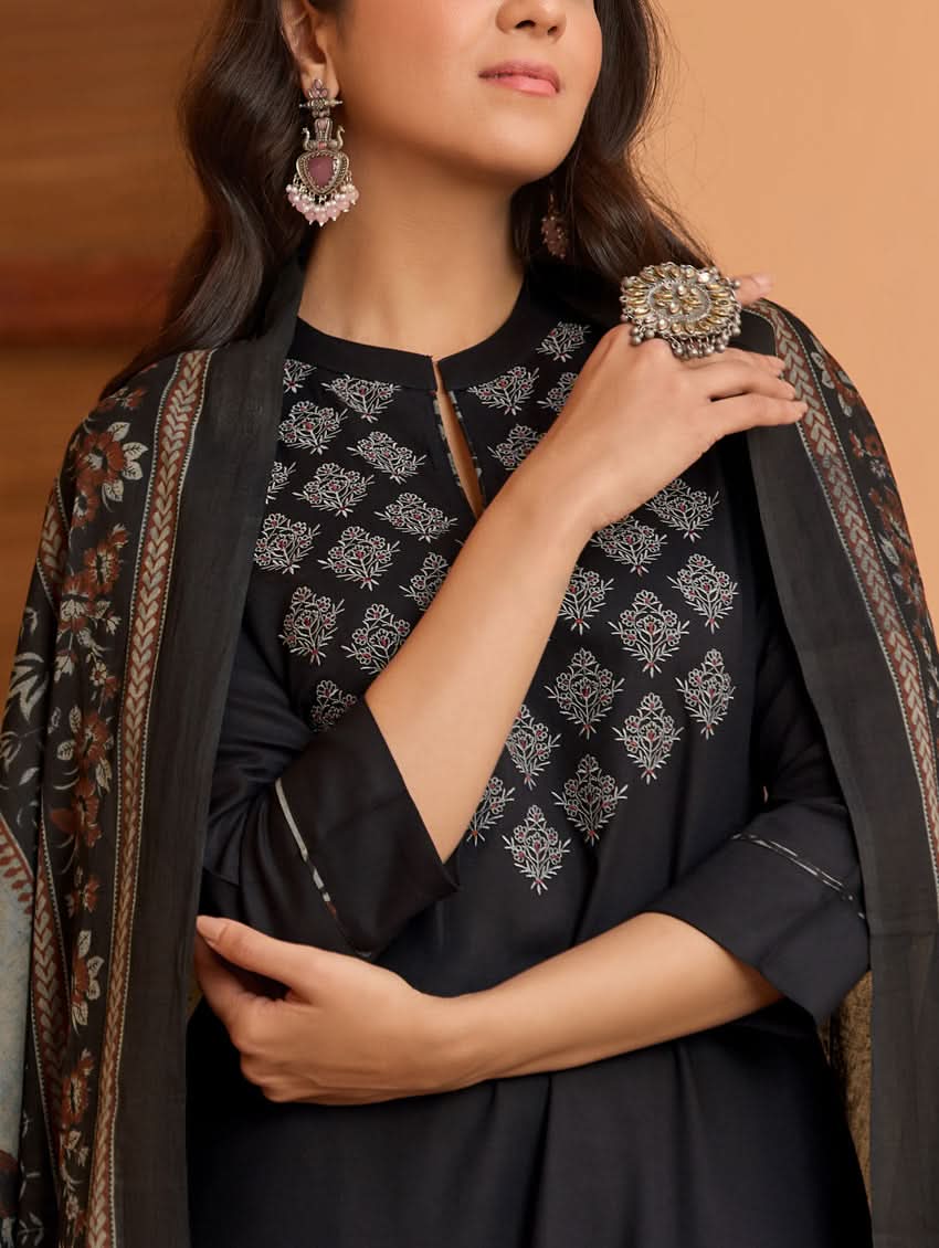 A woman wearing a black kurta with ban collar, three-fourth sleeves, and side slits, paired with black pants and a printed dupatta.