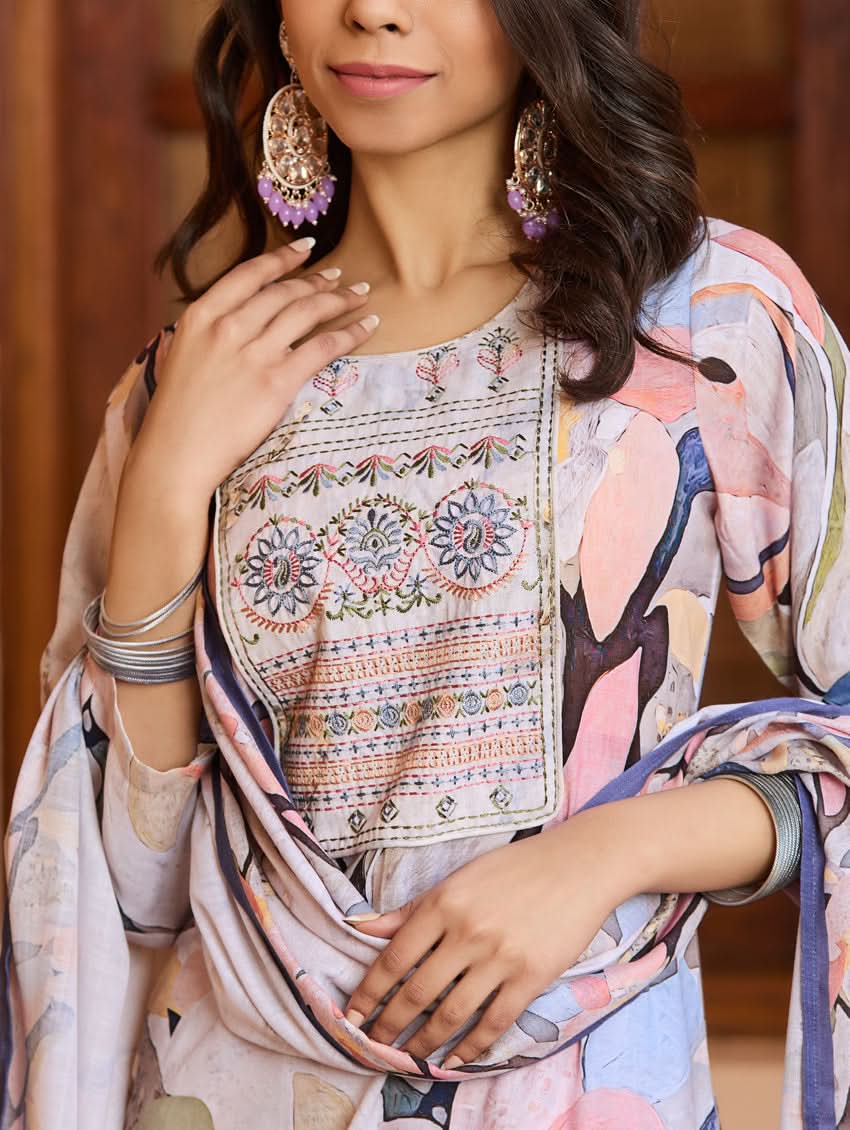 A woman wearing a digitally printed cotton suit set with a kurta, pants, and a dupatta, standing in a room with a wooden background.