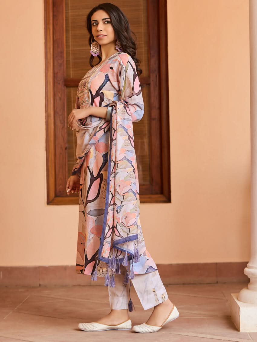 A woman wearing a digitally printed cotton suit set with a kurta, pants, and a dupatta, standing in a room with a wooden background.