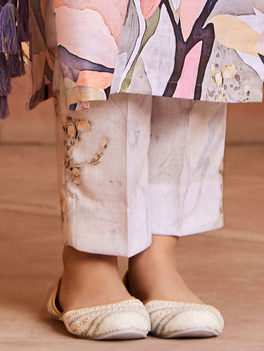 A woman wearing a digitally printed cotton suit set with a kurta, pants, and a dupatta, standing in a room with a wooden background.