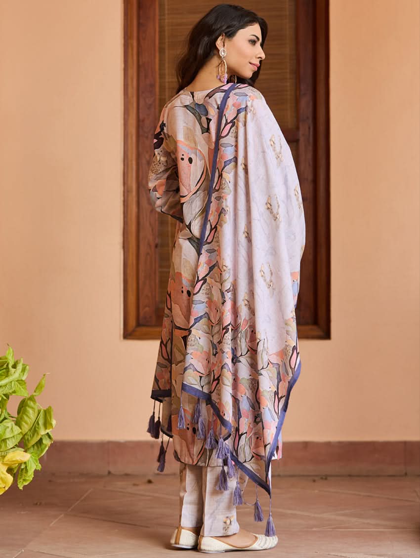 A woman wearing a digitally printed cotton suit set with a kurta, pants, and a dupatta, standing in a room with a wooden background.