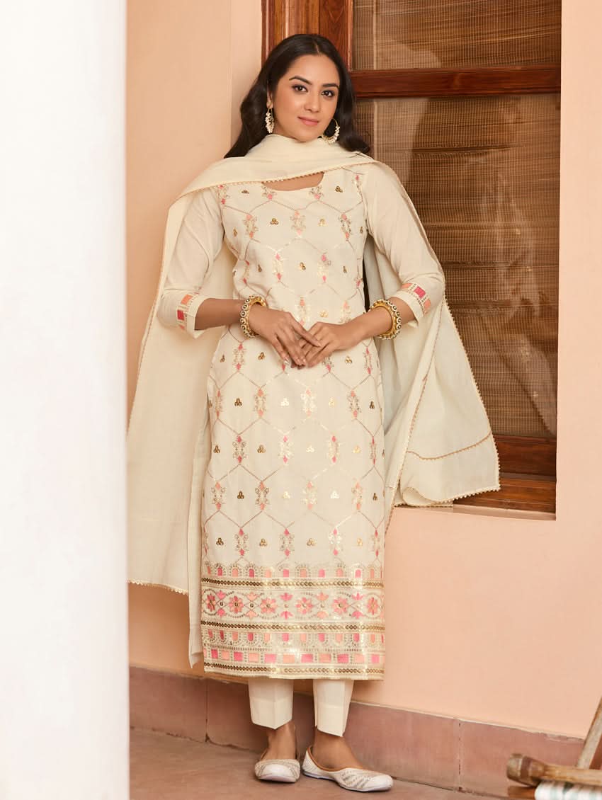 A woman wearing a traditional embroidered cotton suit set with a dupatta, featuring a round neckline and sequin-embroidered details.