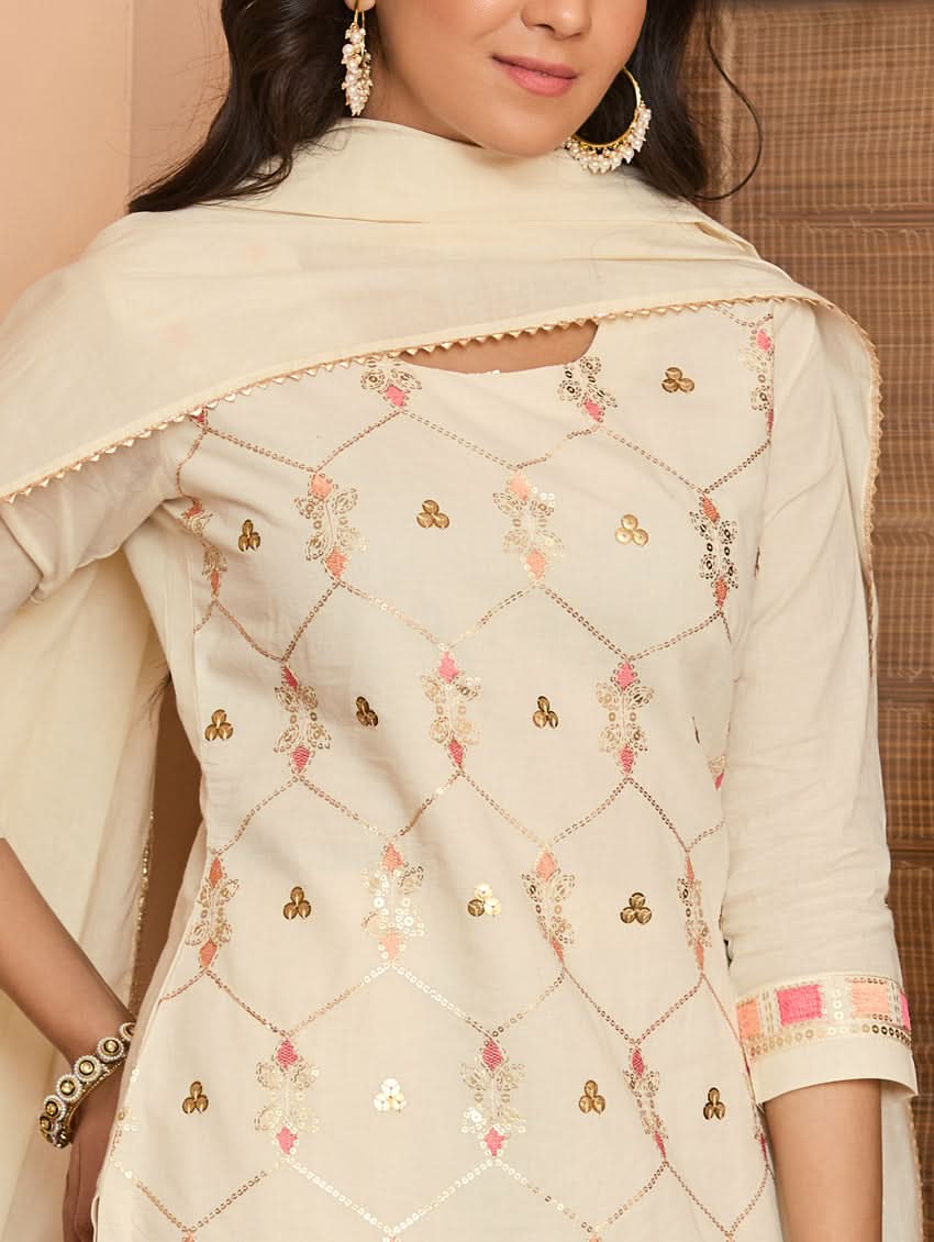A woman wearing a traditional embroidered cotton suit set with a dupatta, featuring a round neckline and sequin-embroidered details.