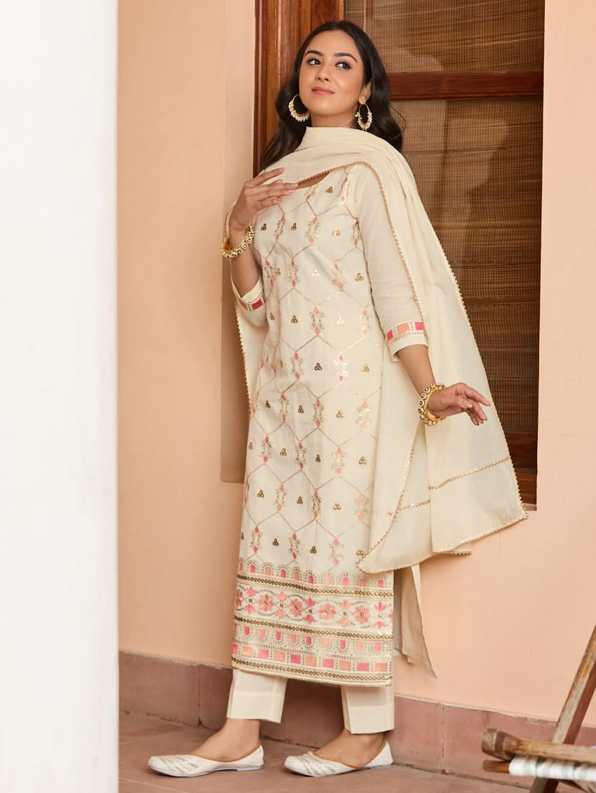 A woman wearing a traditional embroidered cotton suit set with a dupatta, featuring a round neckline and sequin-embroidered details.