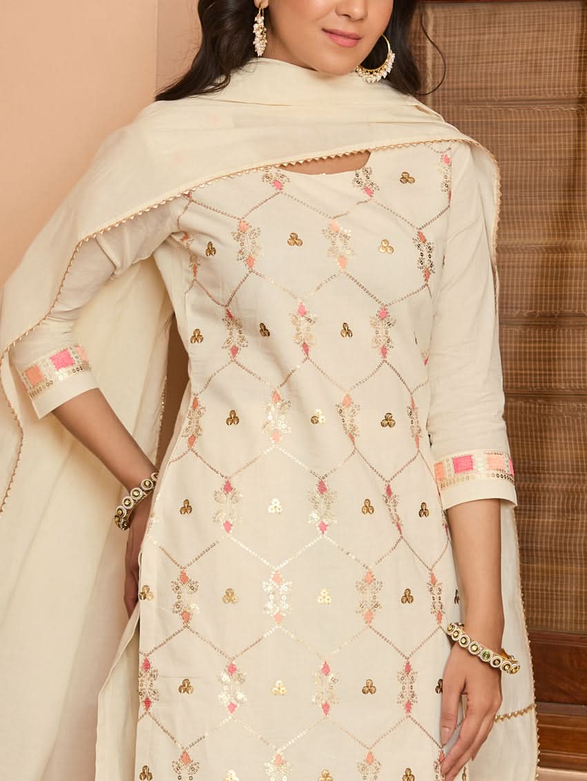A woman wearing a traditional embroidered cotton suit set with a dupatta, featuring a round neckline and sequin-embroidered details.