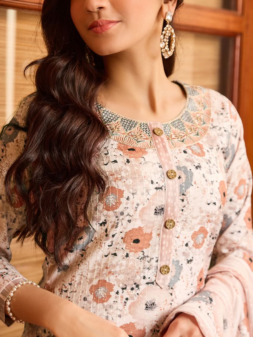 A woman standing in a doorway wearing a traditional white cotton linen suit with floral embroidery, a dupatta over her shoulders, and sandals on her feet.