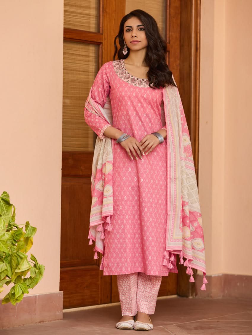 A woman wearing a pink kurta with three-fourth sleeves and side slits, paired with straight pants and a matching dupatta with floral print and tassels.