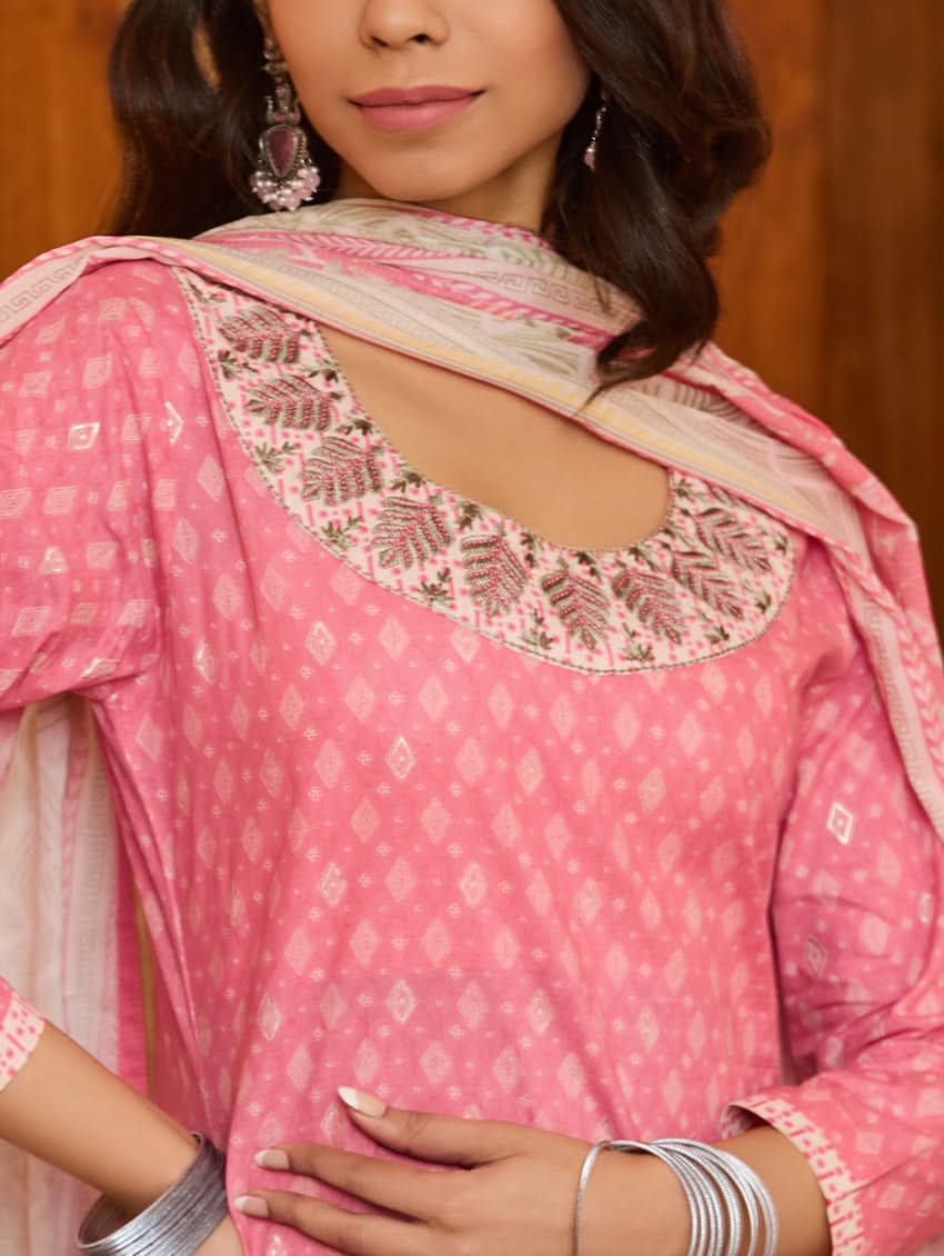 A woman wearing a pink kurta with three-fourth sleeves and side slits, paired with straight pants and a matching dupatta with floral print and tassels.