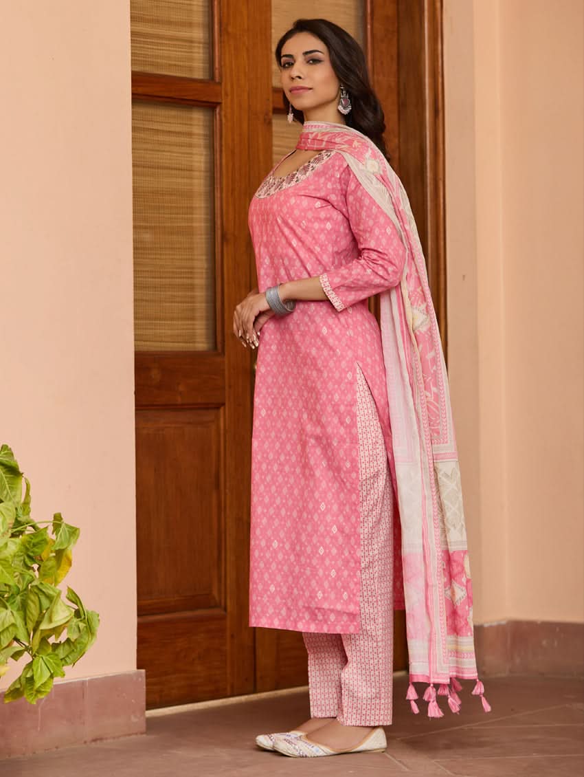 A woman wearing a pink kurta with three-fourth sleeves and side slits, paired with straight pants and a matching dupatta with floral print and tassels.