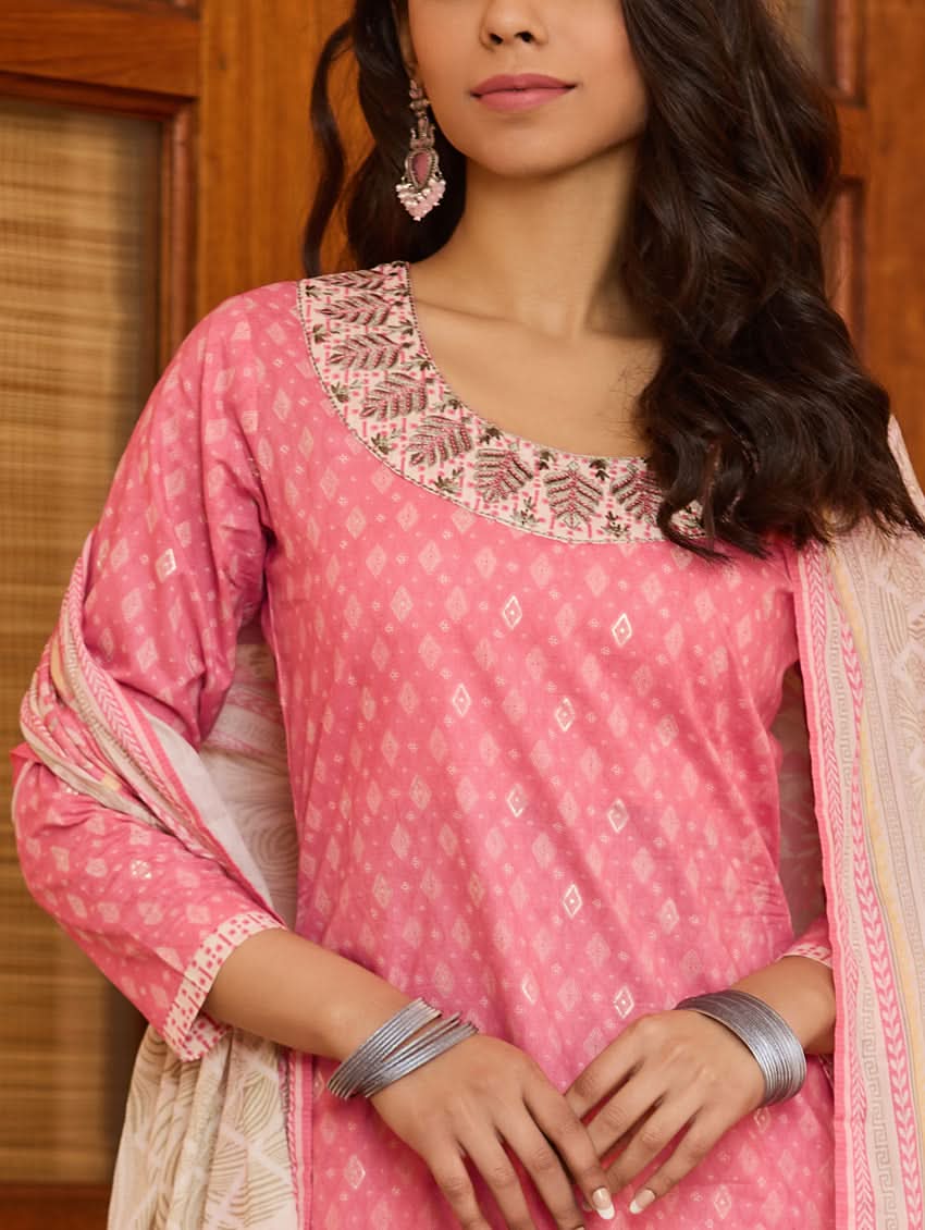 A woman wearing a pink kurta with three-fourth sleeves and side slits, paired with straight pants and a matching dupatta with floral print and tassels.