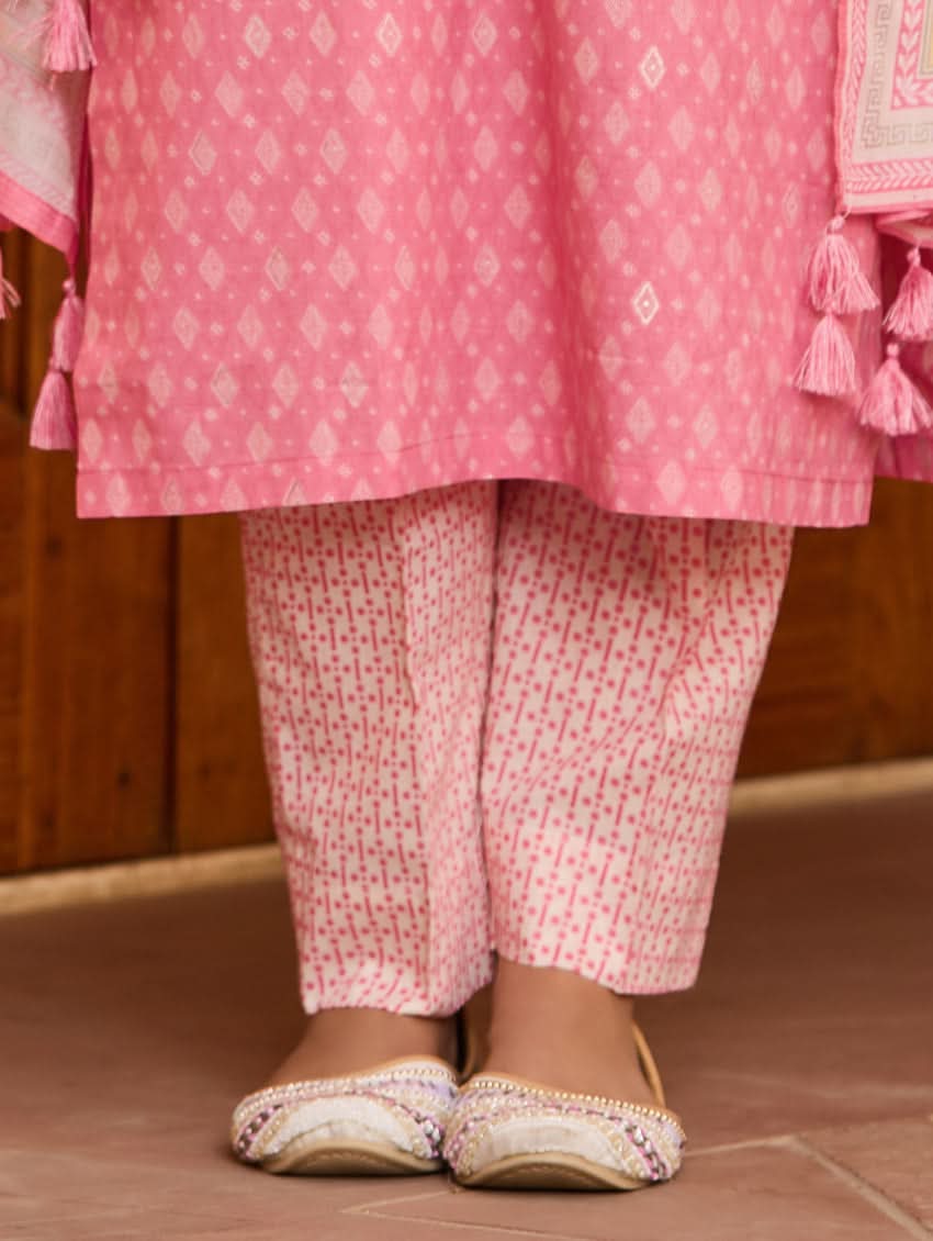 A woman wearing a pink kurta with three-fourth sleeves and side slits, paired with straight pants and a matching dupatta with floral print and tassels.