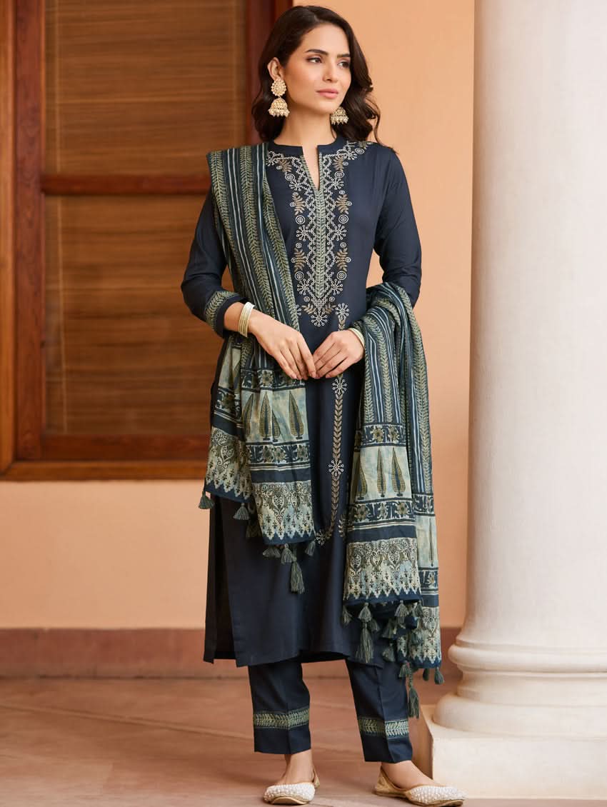 A woman wearing a traditional suit set with embroidered details, consisting of a black kurta with a ban collar, three-fourth sleeves, and side slits, and black pants with a partially elasticated waistband. She is also wearing a printed mul dupatta with the suit set.