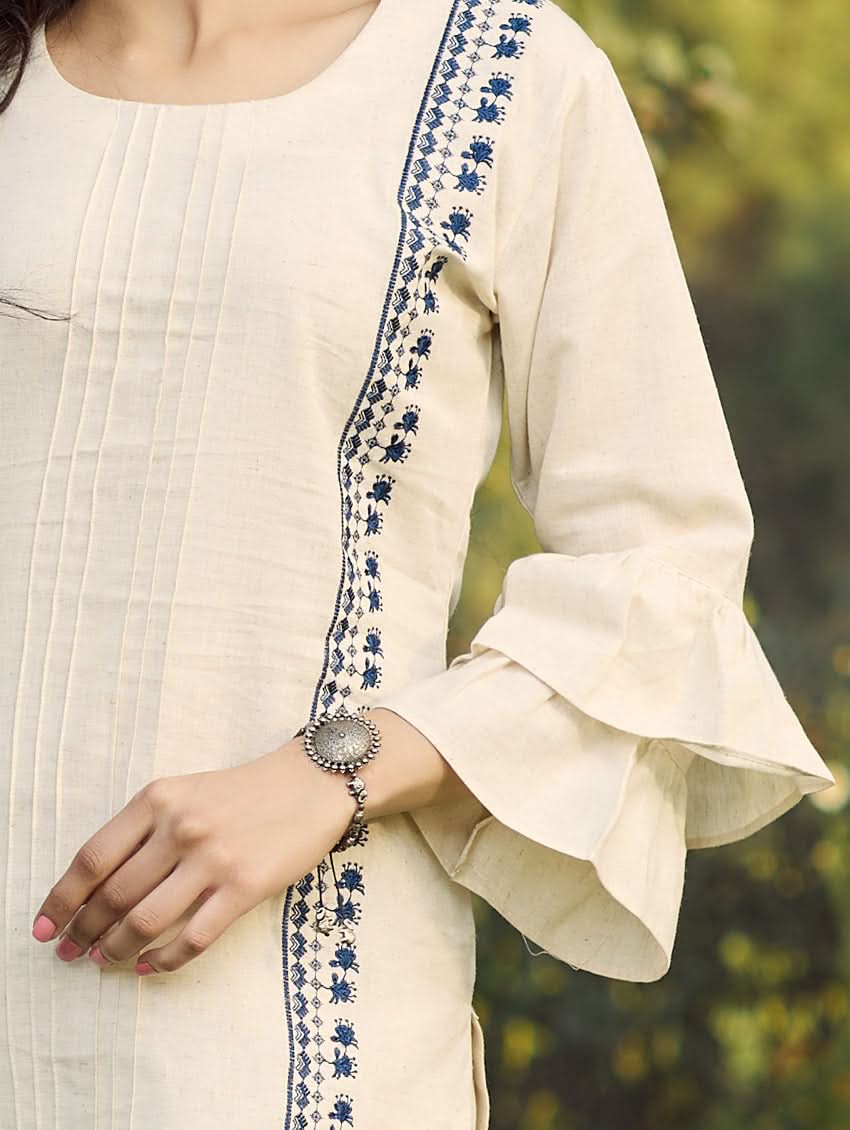 A woman standing outdoors wearing a beige embroidered viscose flex co-ord set with short kurta and pants, next to a pink bicycle.