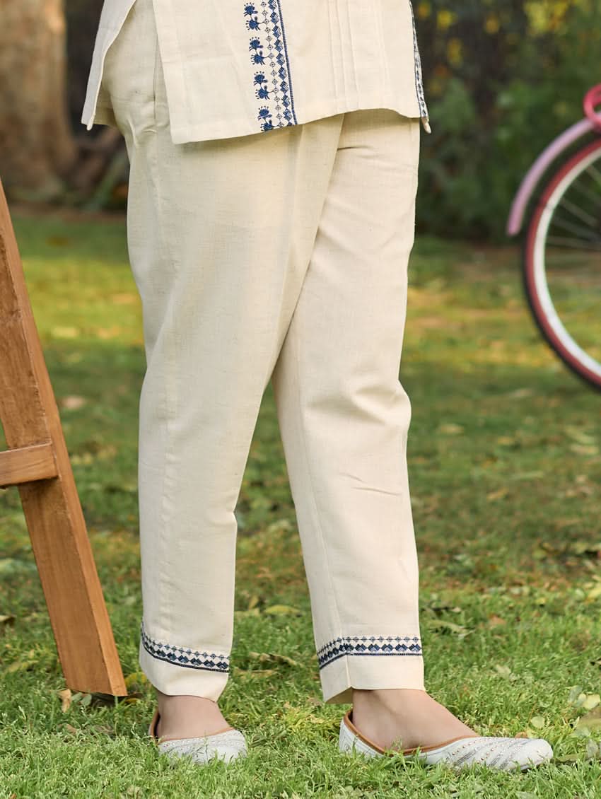 A woman standing outdoors wearing a beige embroidered viscose flex co-ord set with short kurta and pants, next to a pink bicycle.