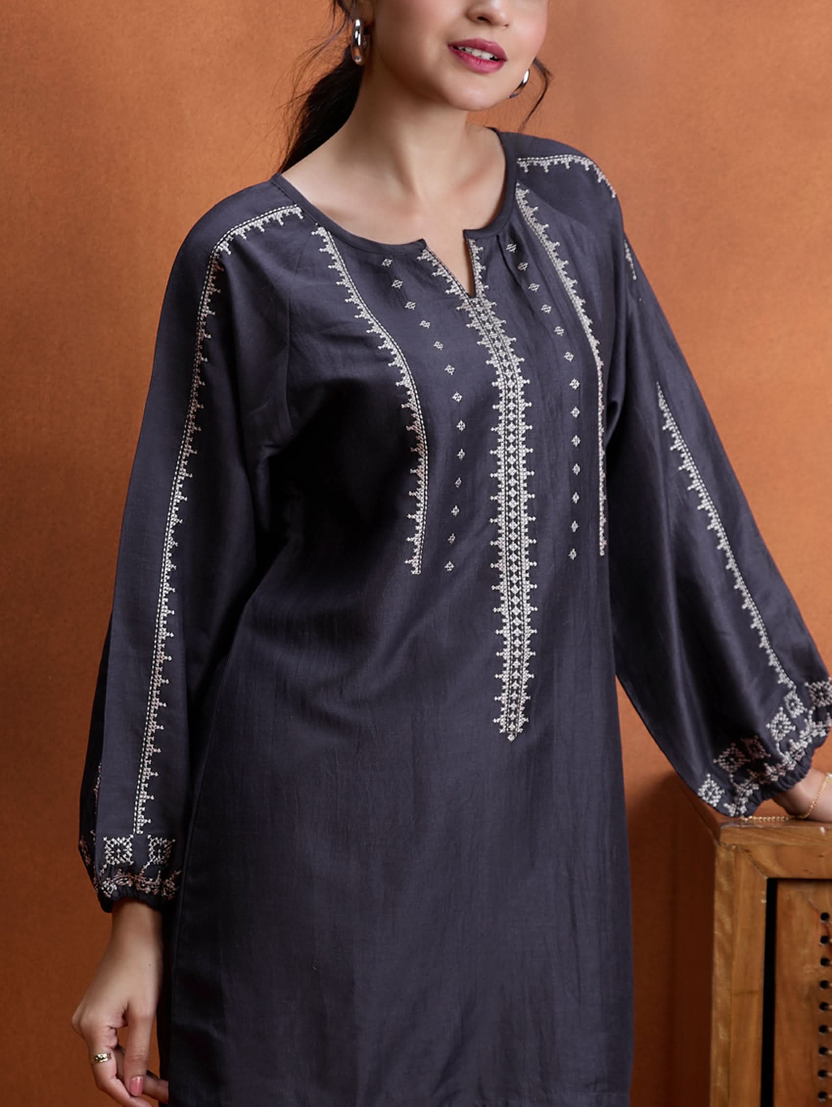 A model wearing a short kurta with a round collar and three-fourth sleeves, paired with pants that have partially elasticated waistband and pockets on either side. The fabric silk blend with computer embroidered