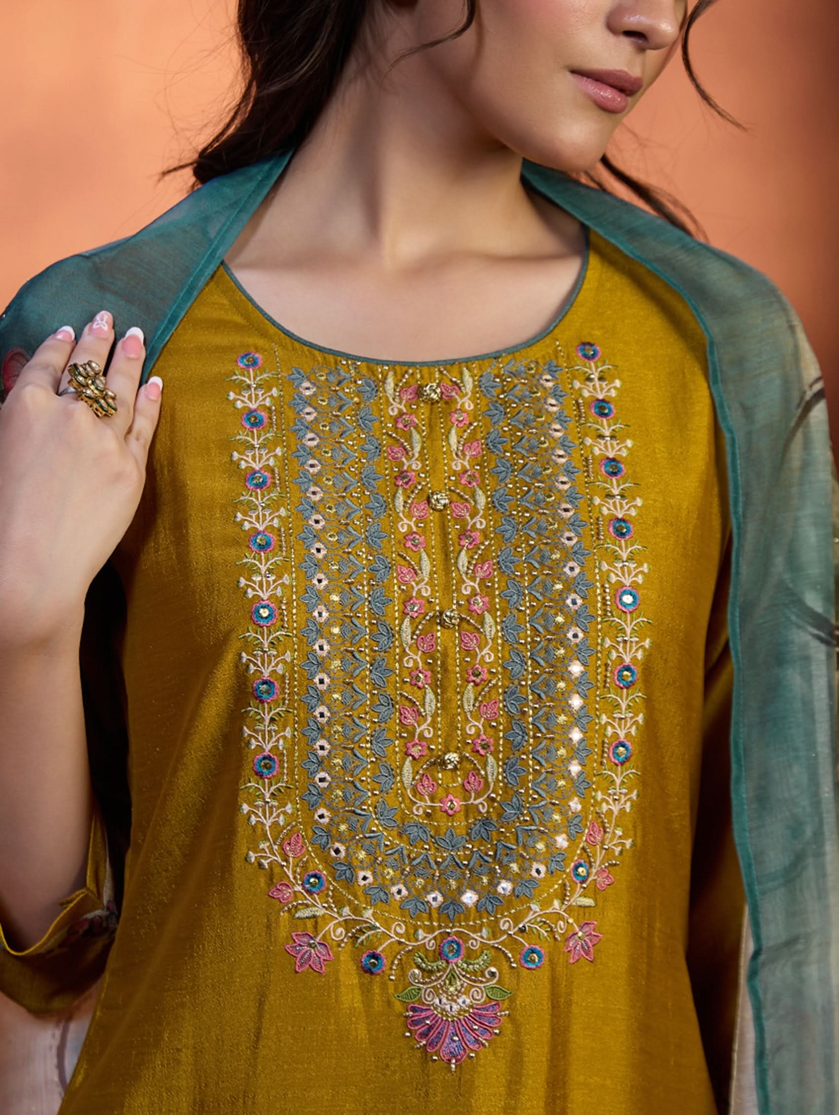 A woman wearing a traditional yellow kurta set with embroidered details and a dupatta with a digital printed chanderi silk design, standing in a room with an orange backdrop.