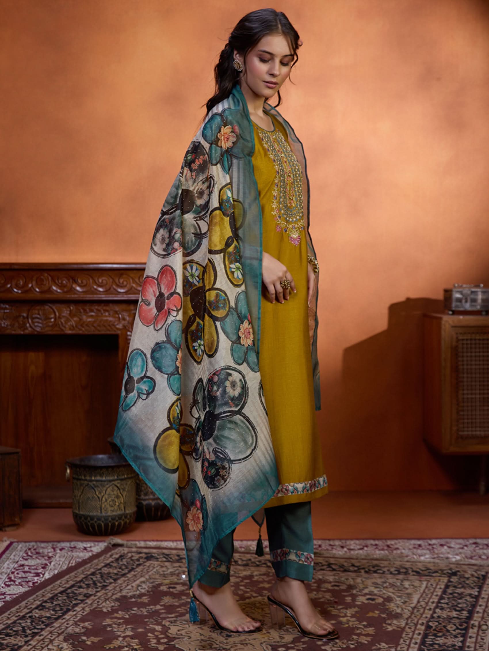 A woman wearing a traditional yellow kurta set with embroidered details and a dupatta with a digital printed chanderi silk design, standing in a room with an orange backdrop.