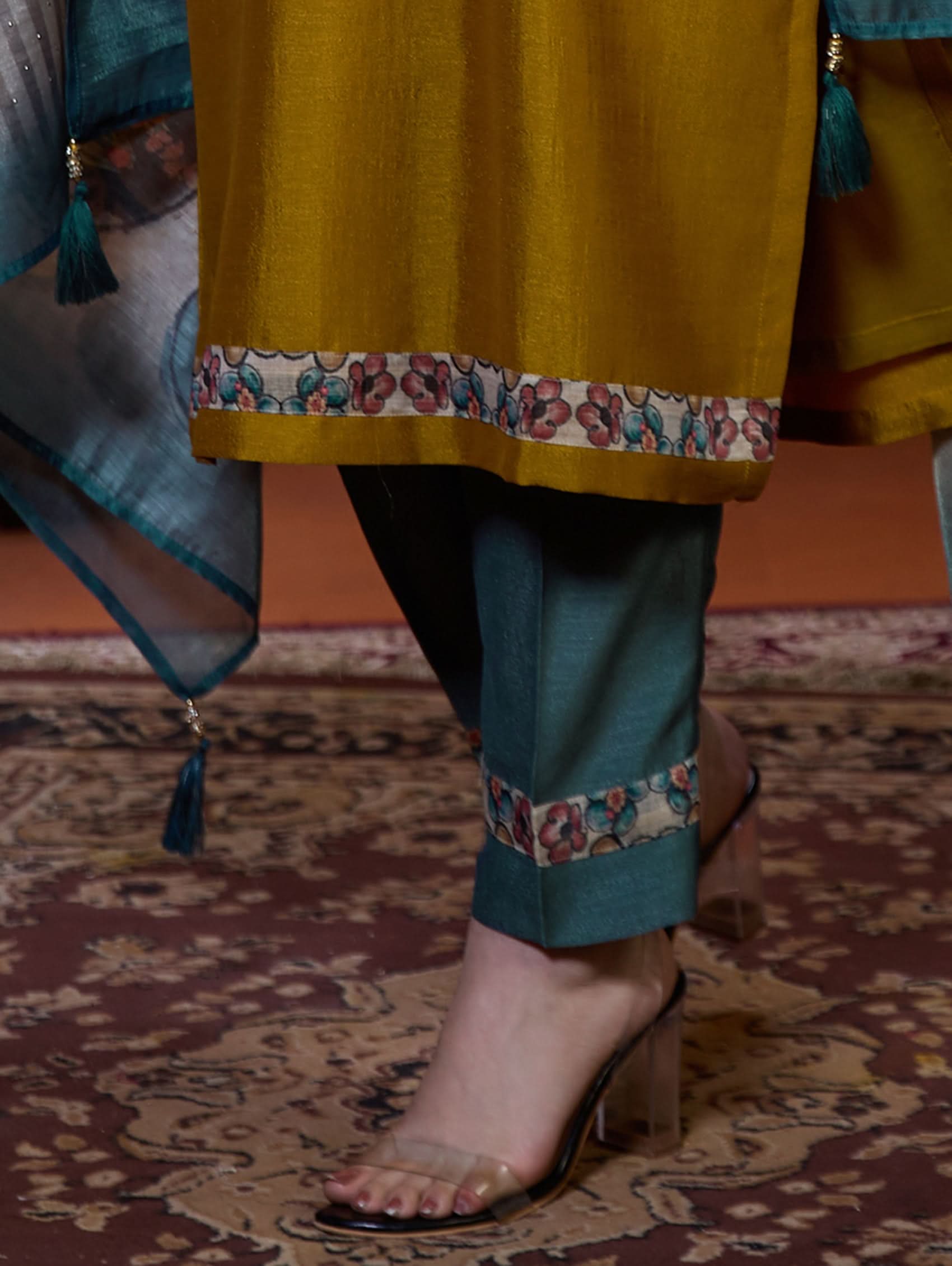 A woman wearing a traditional yellow kurta set with embroidered details and a dupatta with a digital printed chanderi silk design, standing in a room with an orange backdrop.