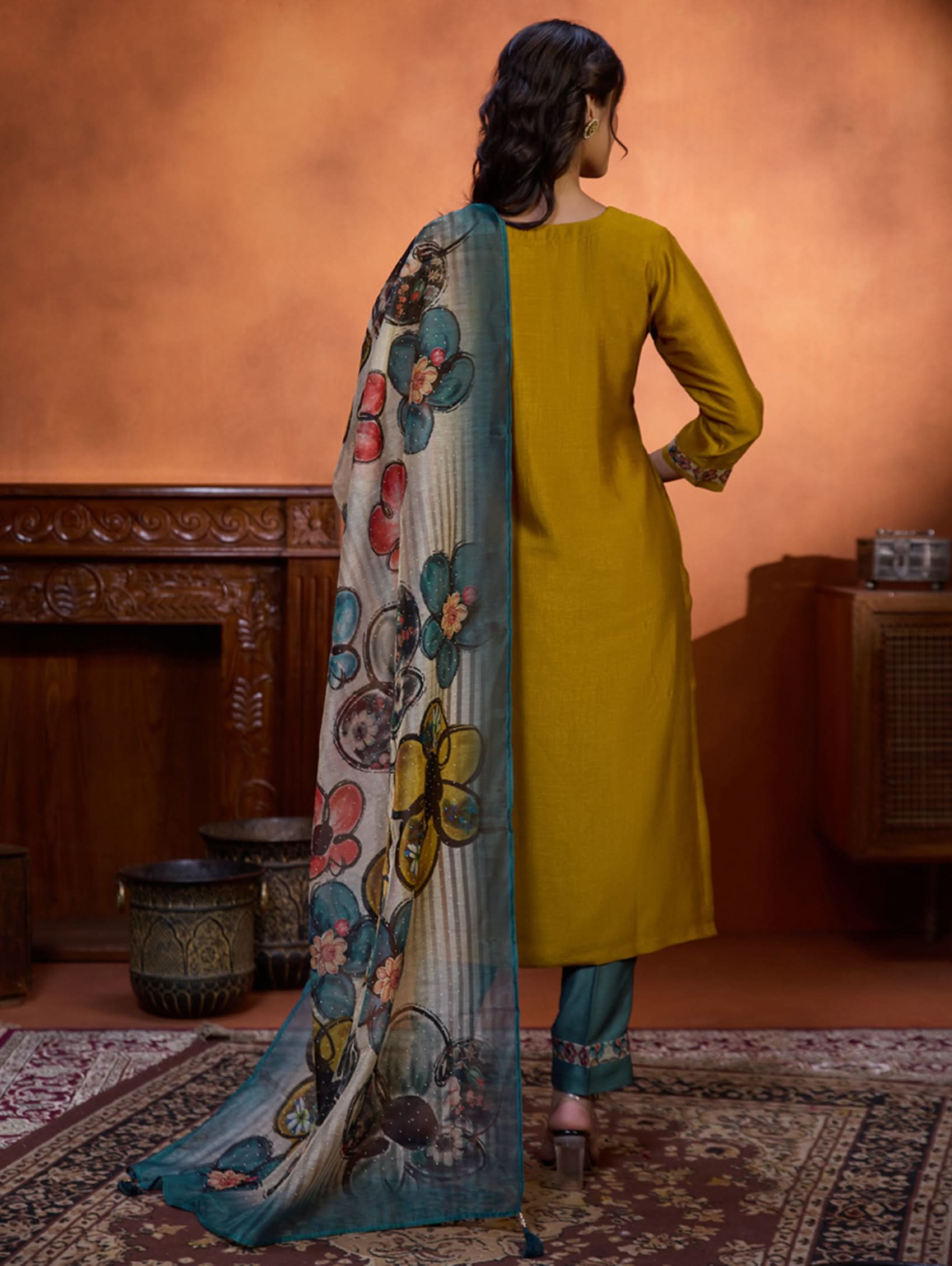 A woman wearing a traditional yellow kurta set with embroidered details and a dupatta with a digital printed chanderi silk design, standing in a room with an orange backdrop.