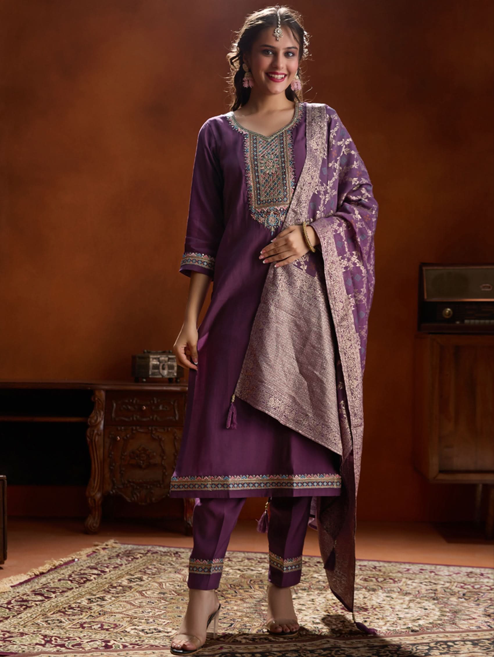 A woman wearing a purple suit set with embroidery, consisting of a kurta, pants, and a dupatta.