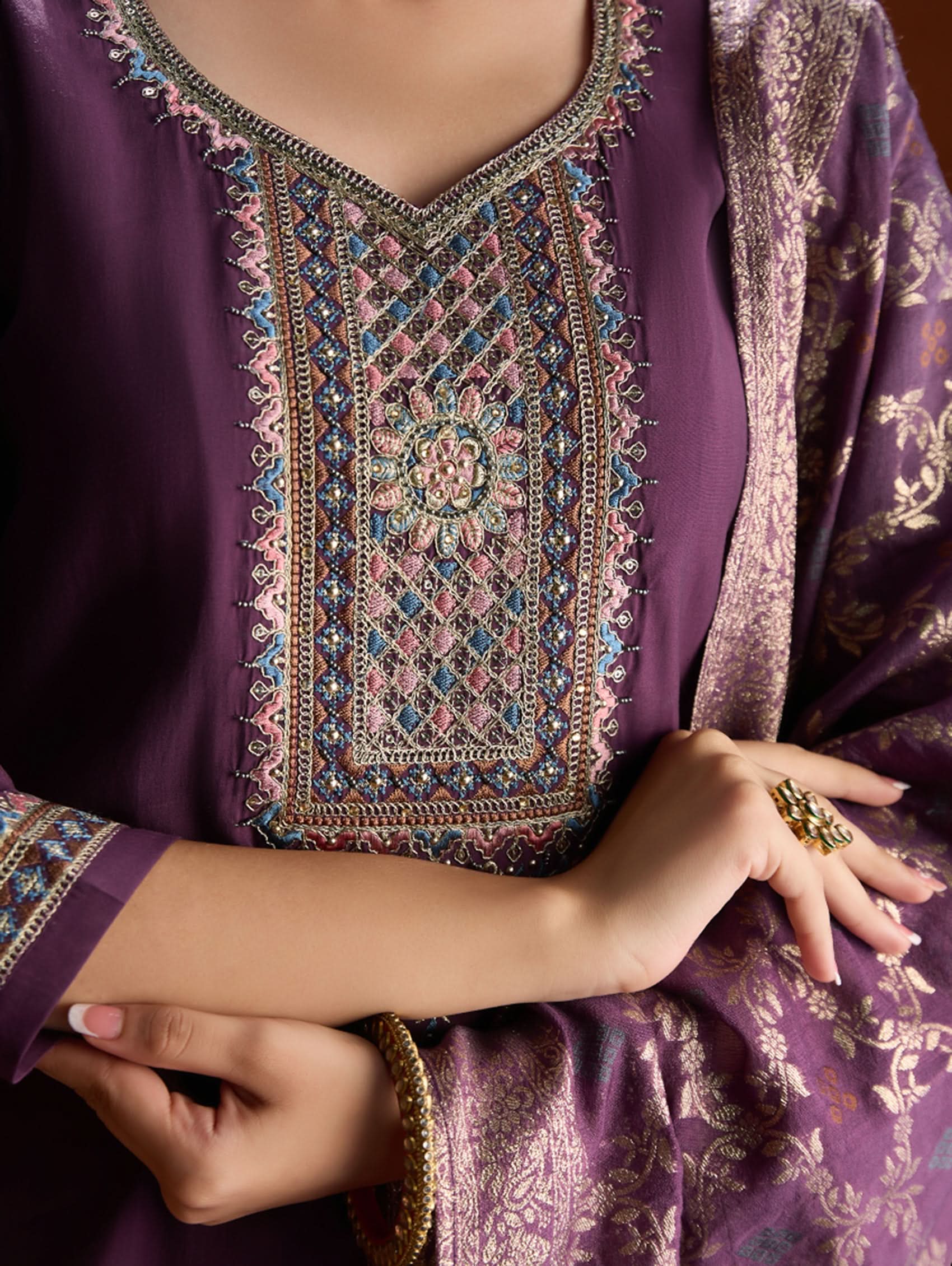 A woman wearing a purple suit set with embroidery, consisting of a kurta, pants, and a dupatta.