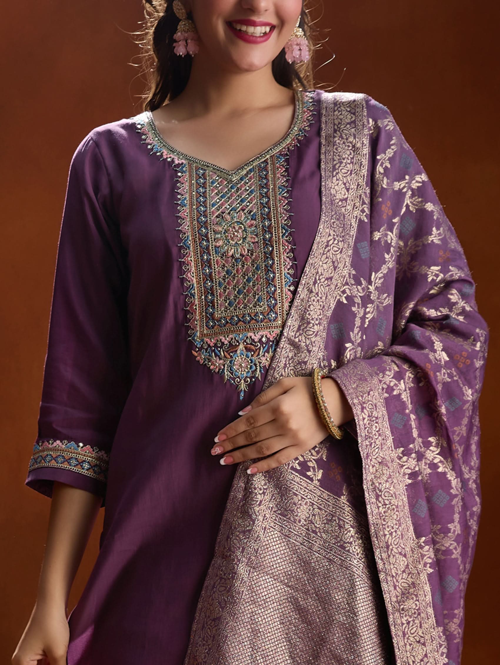 A woman wearing a purple suit set with embroidery, consisting of a kurta, pants, and a dupatta.
