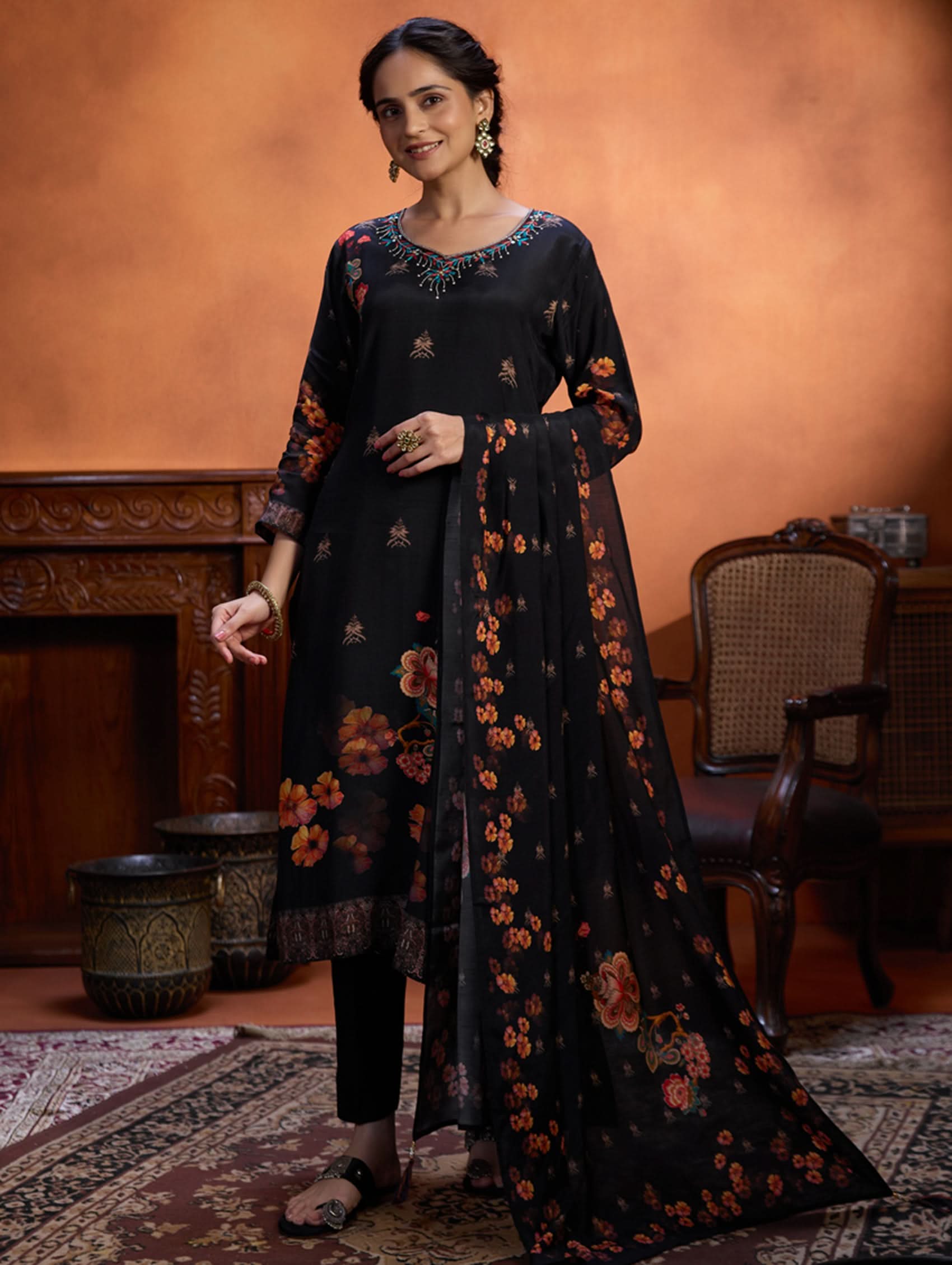 Woman wearing a black floral outfit in an indoor setting with a warm-toned wall.
