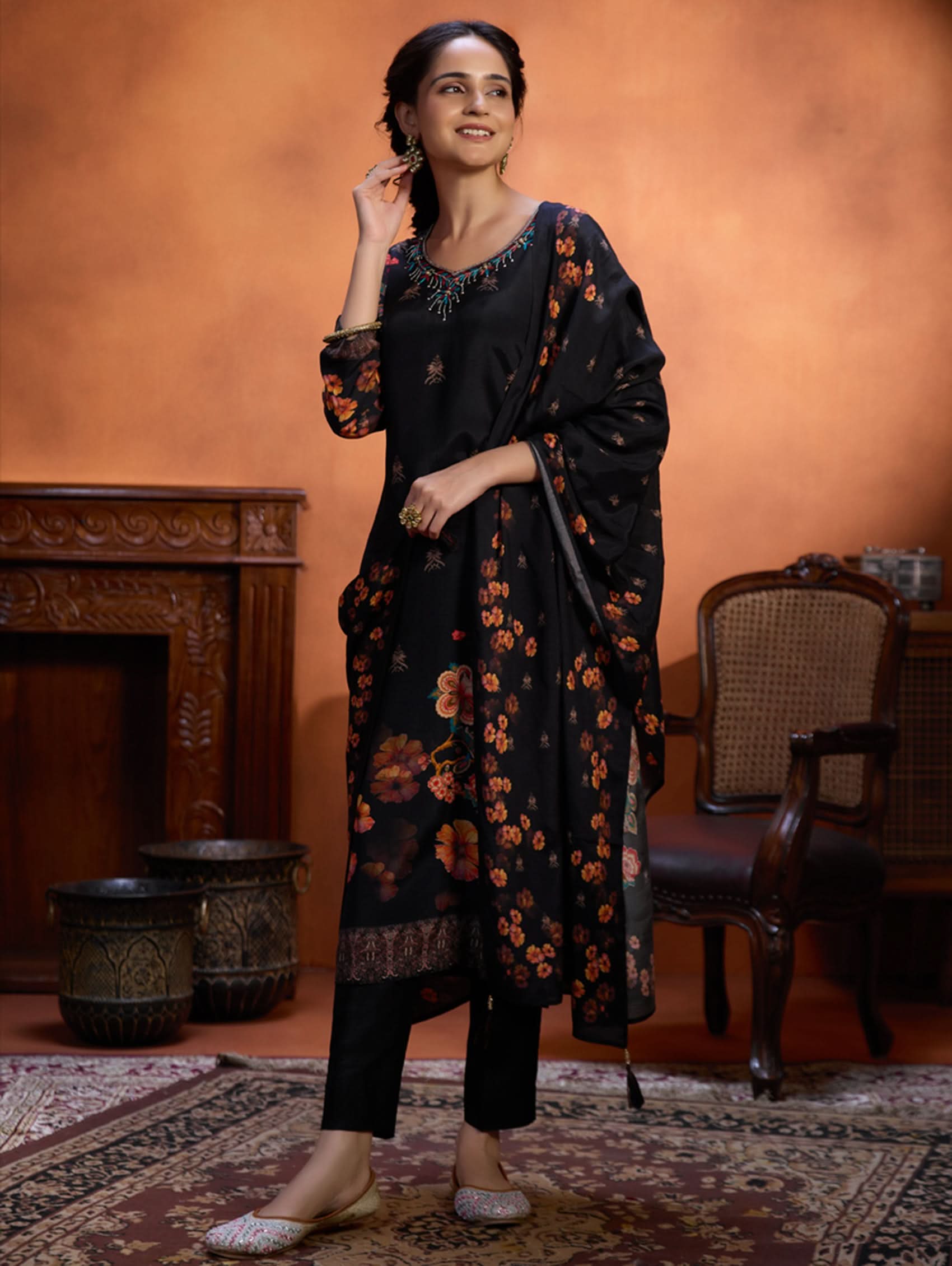 Woman in a black floral outfit standing in an elegant room with wooden furniture and a warm color palette.